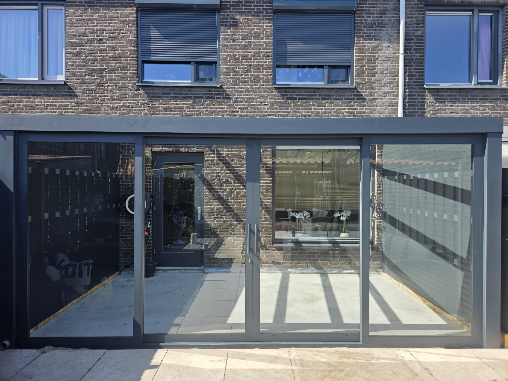 Aluminium veranda met glazen schuifwanden langs woninggevel
